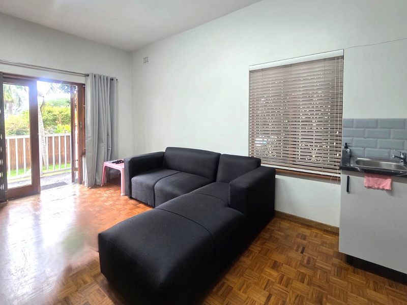 Open plan living area featuring parquet flooring, a compact kitchenette with subway tile backsplash, and direct access to an outdoor patio area.