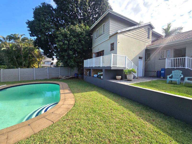 Rear exterior view of the cottage featuring a swimming pool, raised patio area with white railings, and a landscaped garden with perimeter fencing.
