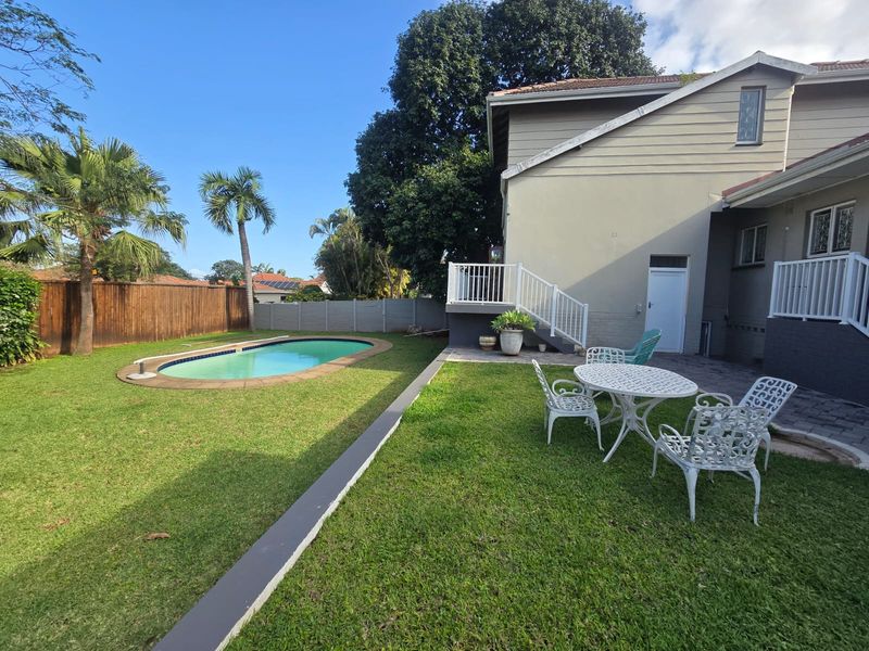 Rear garden featuring a swimming pool, paved patio area, raised deck with white railings, and established lawn enclosed by boundary fencing.