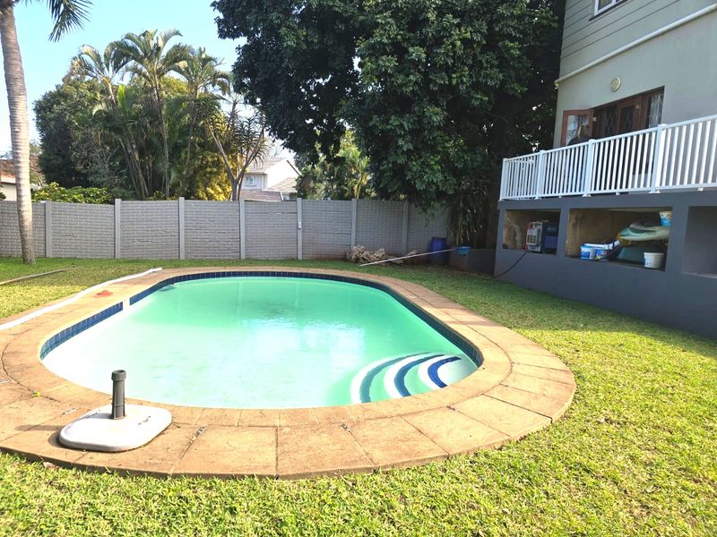 A backyard pool area featuring a swimming pool, surrounding lawn, and a raised deck with white railing attached to the main cottage structure.
