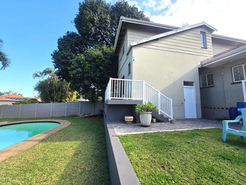 Rear exterior view of the cottage featuring a swimming pool, raised deck with railing, paved patio area, and a private garden.