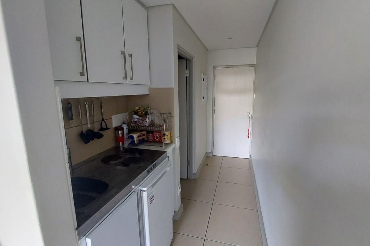 A compact kitchen area featuring built-in cabinetry, a hob, and a sink, leading into a hallway with tiled flooring.