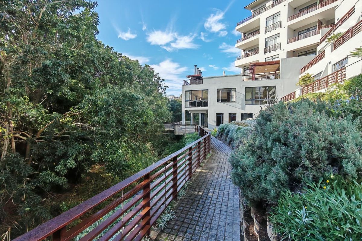 A well-maintained exterior rear view of the apartment complex featuring a paved walkway, timber balustrades, and landscaped garden areas.