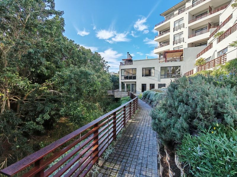 A well-maintained exterior rear view of the apartment complex featuring a paved walkway, timber balustrades, and landscaped garden areas.
