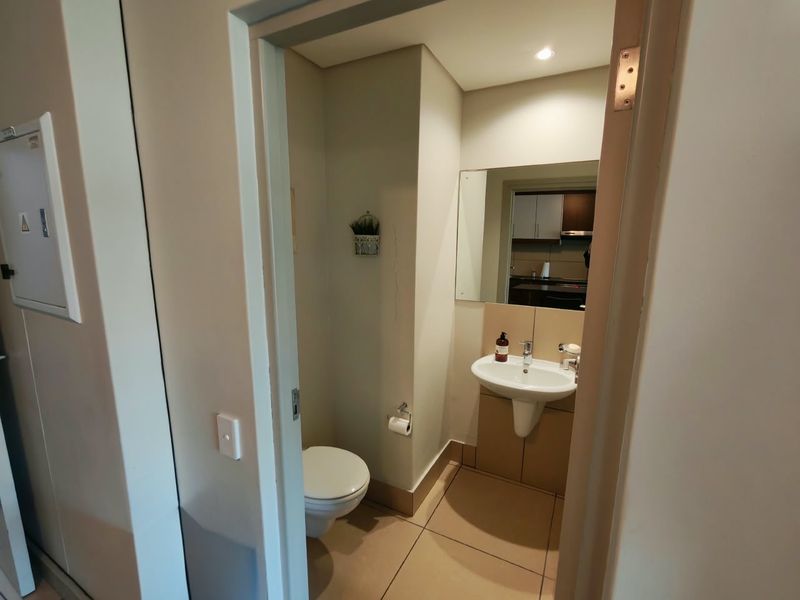 A compact guest bathroom featuring a pedestal basin, toilet, and wall-mounted mirror with neutral floor tiling.