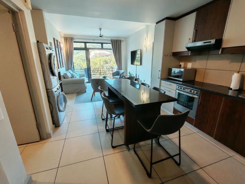 Modern open-plan living area featuring a well-equipped kitchen with built-in cabinetry, a central island, and seamless flow to a balcony with scenic views.