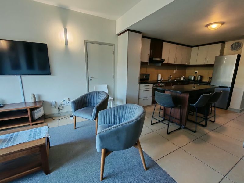 Open plan living area featuring a modern kitchen with a central island, tiled flooring, and integrated cabinetry, seamlessly connecting to the lounge space.