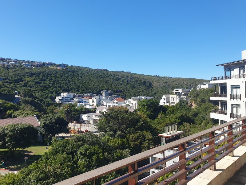 Elevated view from a balcony overlooking a lush green hillside and surrounding residential neighborhood.