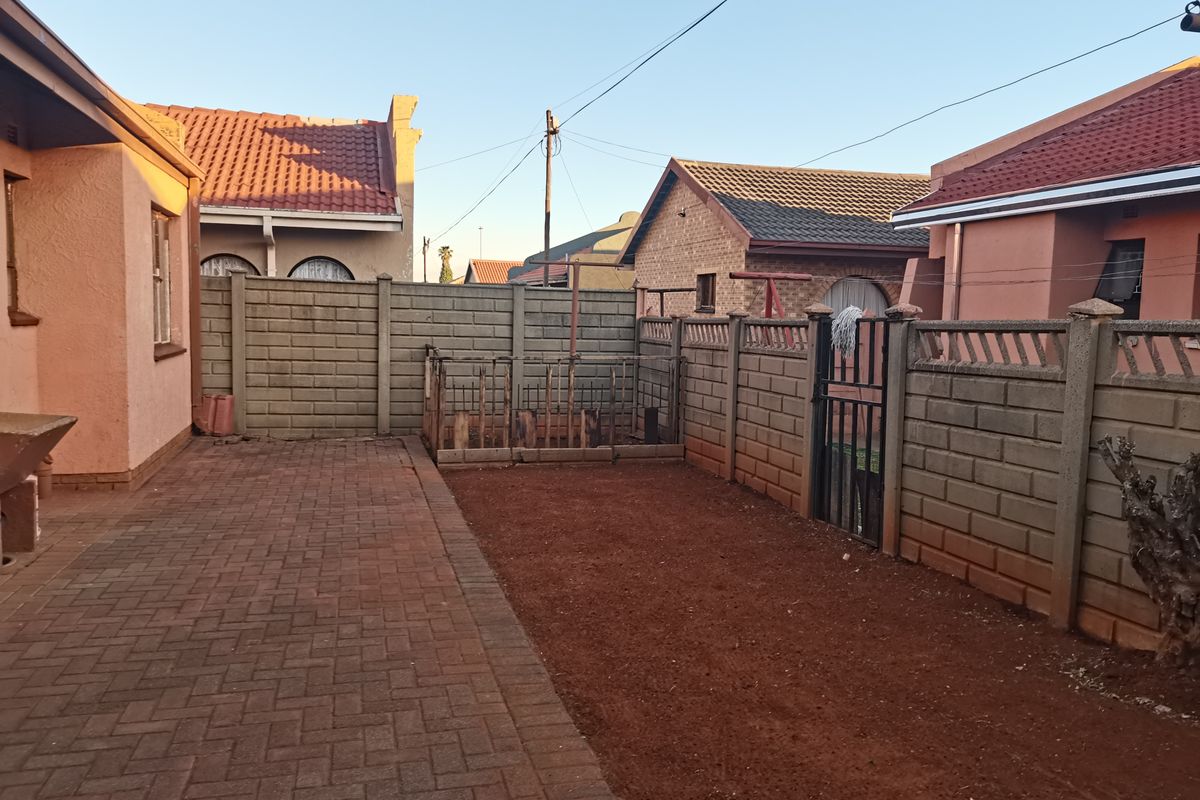A rear exterior view showing a paved patio area, precast concrete boundary walls, and an unlandscaped soil section between neighbouring properties.