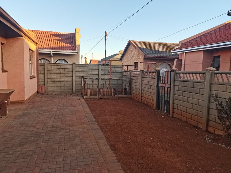 A rear exterior view showing a paved patio area, precast concrete boundary walls, and an unlandscaped soil section between neighbouring properties.