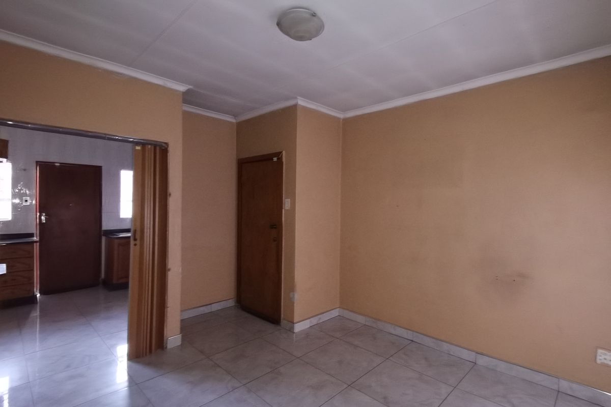 An empty living room featuring tiled flooring, neutral wall paint, and a folding door leading to an adjacent kitchen area.