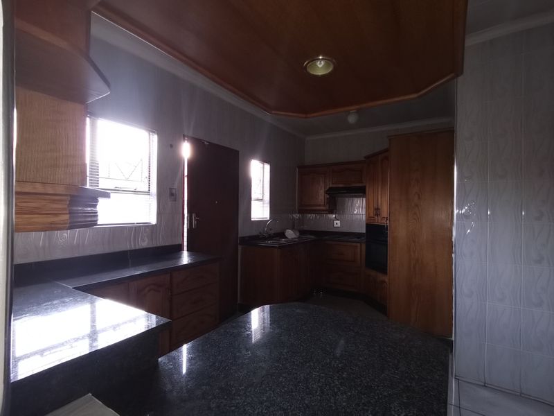 A spacious kitchen featuring dark granite countertops, extensive wooden cabinetry, built-in oven, and tiled finishes throughout.