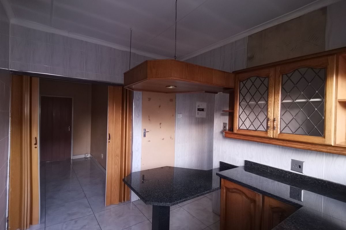 Kitchen featuring granite countertops, wooden cabinetry with glass detailing, and tiled finishes. The space is vacant and ready for modernization.