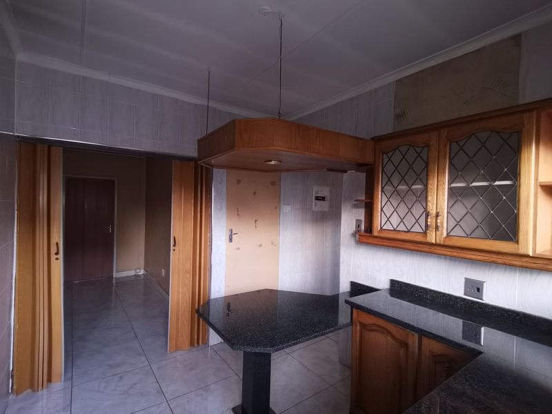 Kitchen featuring granite countertops, wooden cabinetry with glass detailing, and tiled finishes. The space is vacant and ready for modernization.