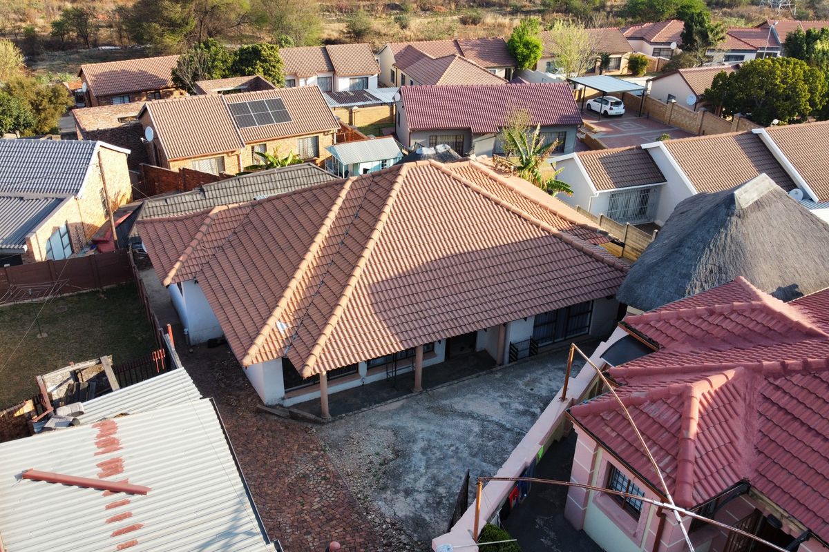 Aerial view of a residential property featuring a tiled roof, covered patio area, and paved driveway within a suburban neighborhood setting.