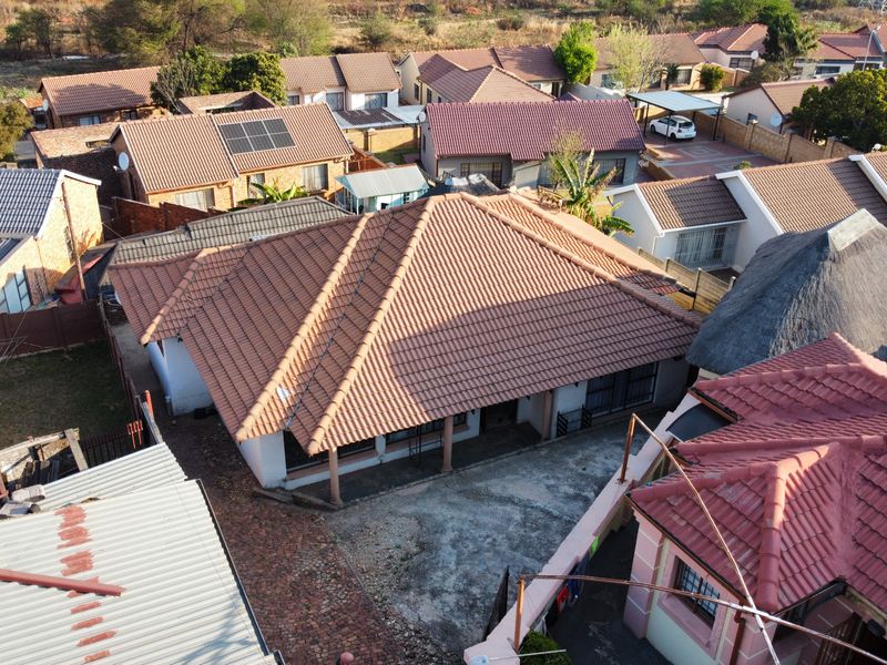 Aerial view of a residential property featuring a tiled roof, covered patio area, and paved driveway within a suburban neighborhood setting.