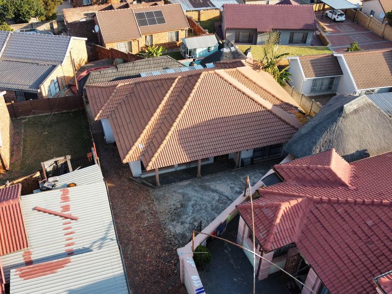 An aerial view of the property showing the main house with a tiled roof, a paved driveway, and surrounding residential structures.
