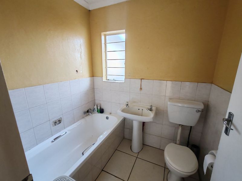 A dated bathroom featuring a standard bathtub, pedestal basin, and toilet with tiled finishes, requiring cosmetic updates to modernize the space.