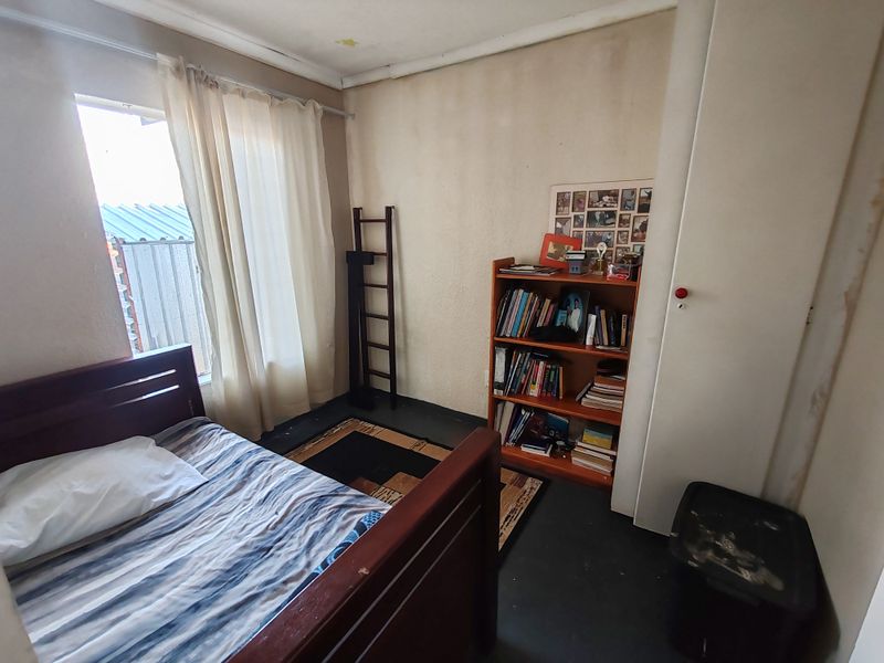 A compact bedroom featuring a built-in wardrobe and natural light, currently requiring cosmetic updates to the walls and ceiling finishes.