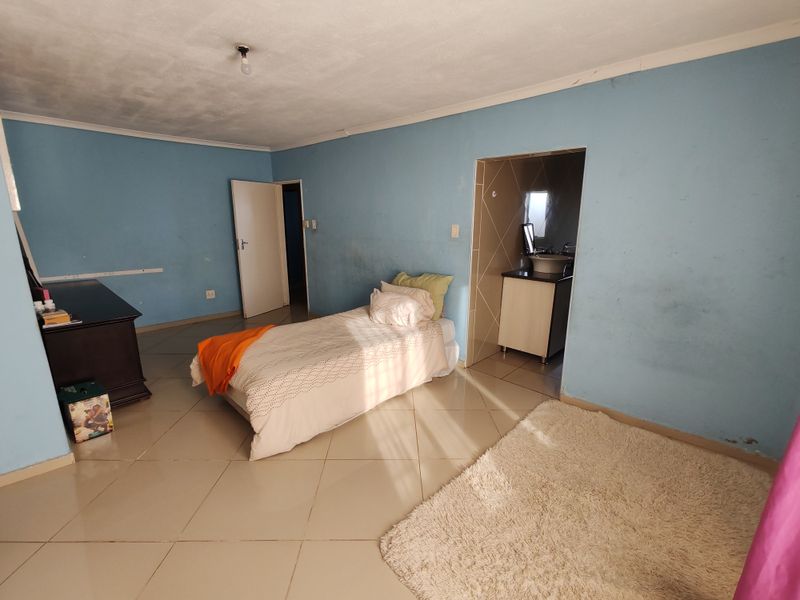 A bedroom featuring tiled flooring and an attached en-suite bathroom with a vanity basin. The room requires cosmetic updates to the wall finishes.