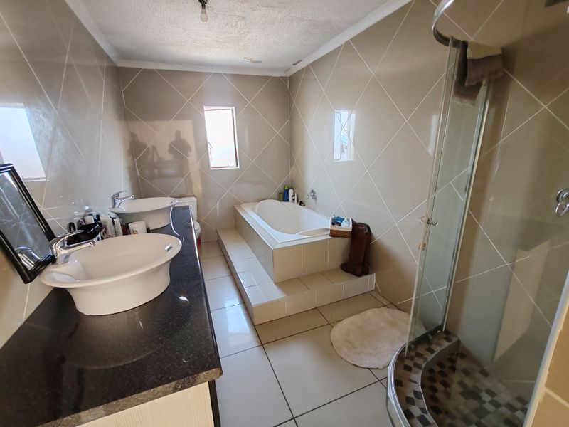 A functional bathroom featuring a double vanity, built-in bathtub, and a separate shower enclosure with tiled finishes throughout.
