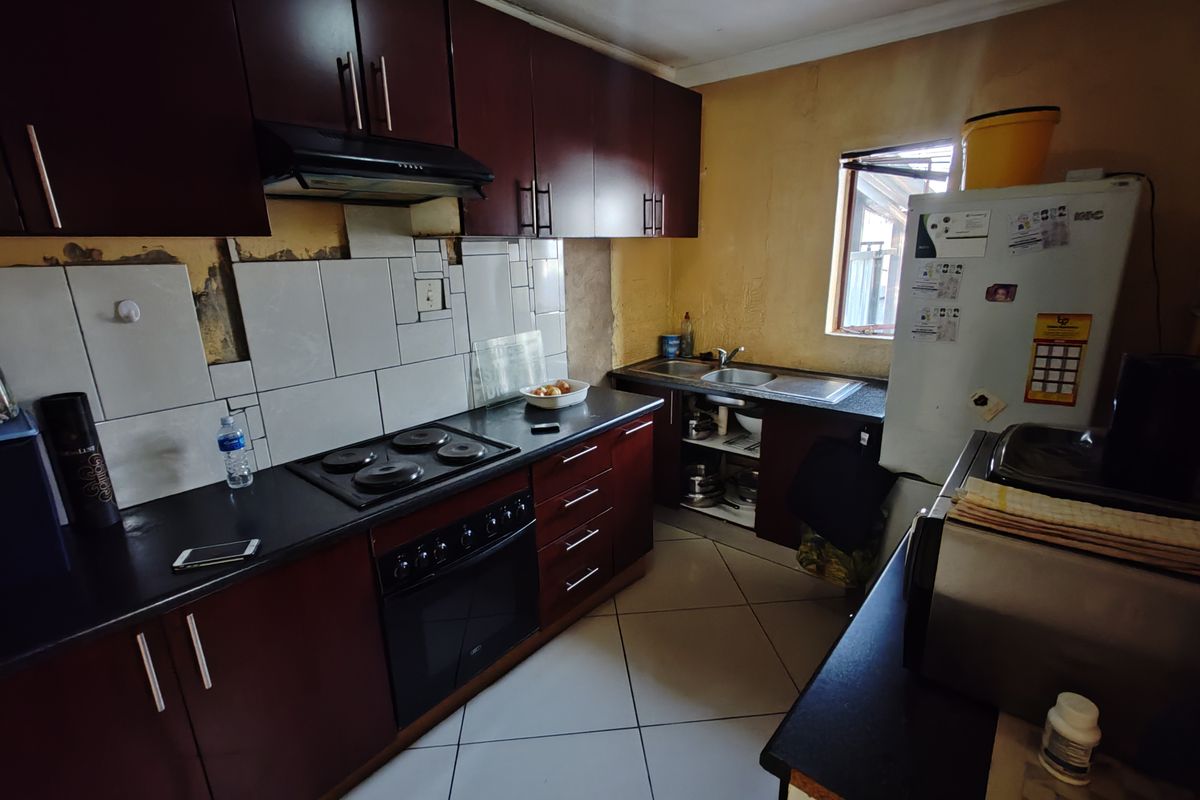 A functional kitchen featuring dark wood cabinetry, built-in oven, electric hob, and tiled splashback, currently requiring cosmetic updates to wall finishes and surfaces.