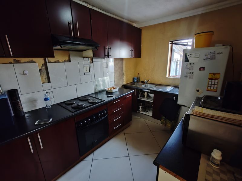 A functional kitchen featuring dark wood cabinetry, built-in oven, electric hob, and tiled splashback, currently requiring cosmetic updates to wall finishes and surfaces.