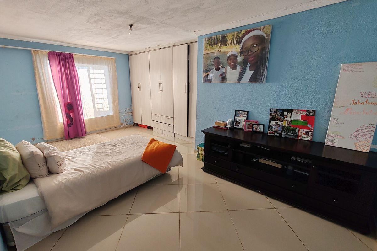 Spacious bedroom featuring built-in cupboards and tiled flooring, requiring some maintenance to address wall dampness and paint deterioration.