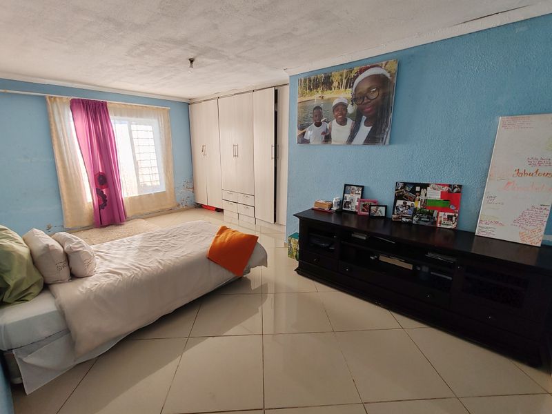 Spacious bedroom featuring built-in cupboards and tiled flooring, requiring some maintenance to address wall dampness and paint deterioration.