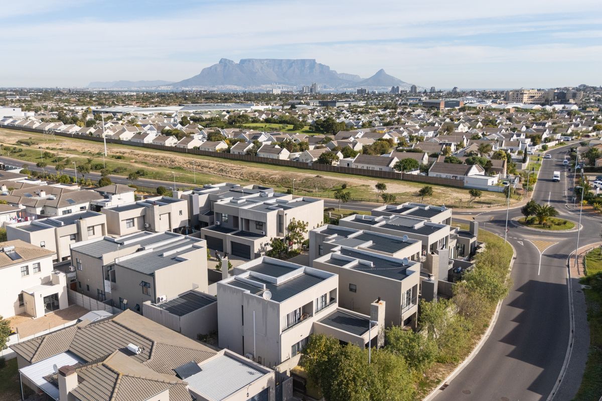 Aerial view of a modern residential estate featuring contemporary flat-roofed townhouses with solar installations and scenic mountain views in the background.