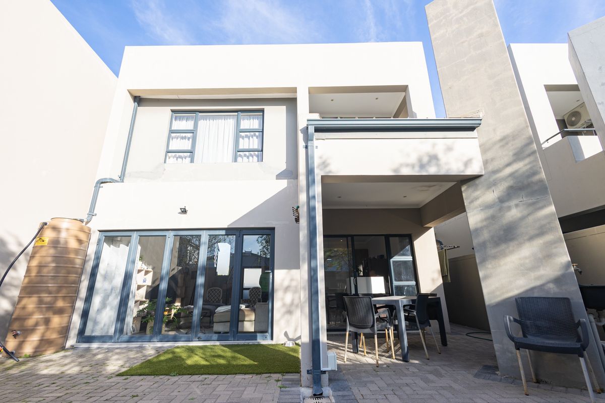 Rear view of a modern two-story house featuring a paved courtyard, covered patio area, and large sliding glass doors providing indoor-outdoor flow.