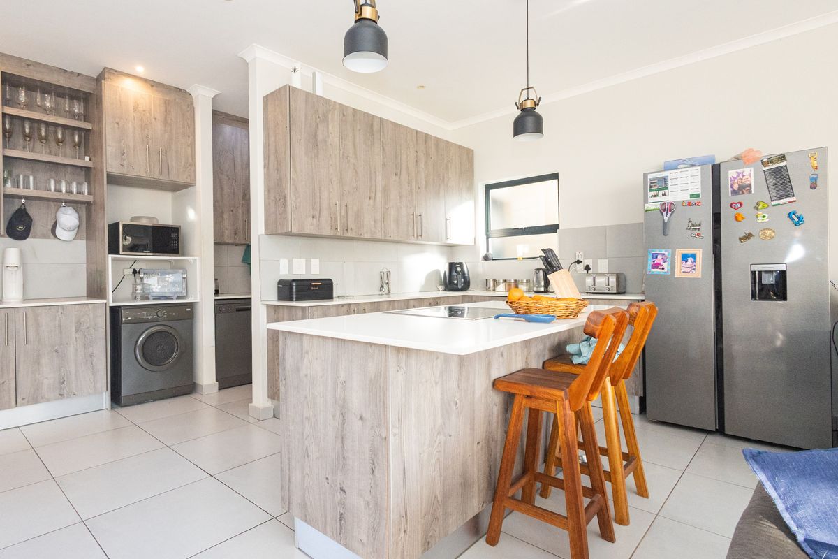 Modern kitchen featuring wood-grain cabinetry, a central island with stone countertops, pendant lighting, and tiled flooring, offering a functional and contemporary cooking space.