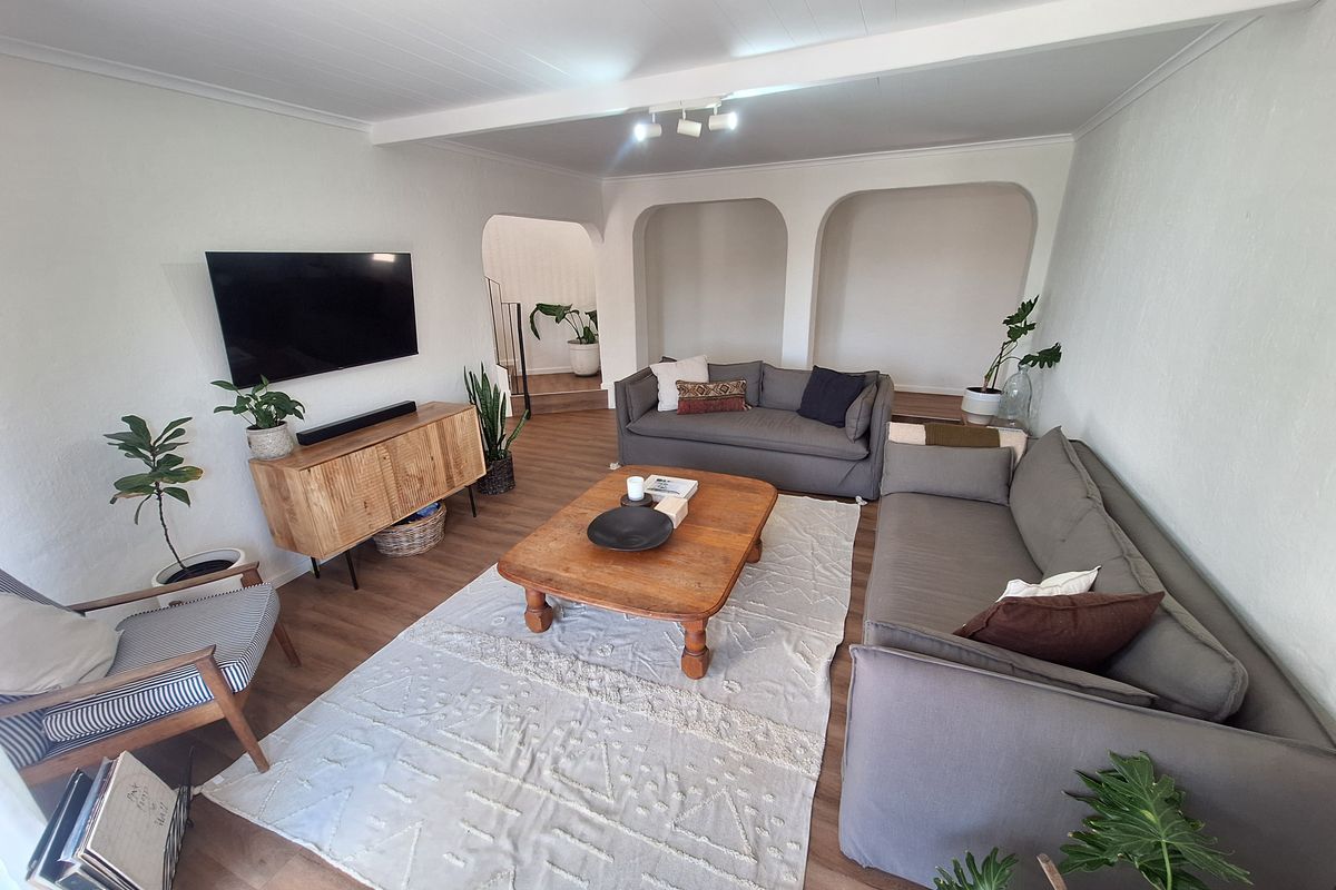 A bright and inviting living room featuring laminate flooring, distinctive arched wall niches, and exposed ceiling beams, creating a comfortable and character-filled living space.