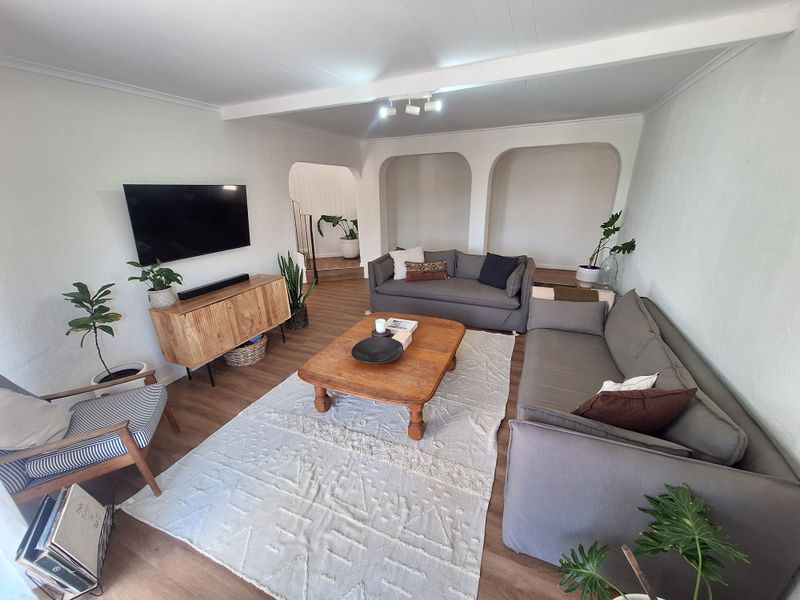 A bright and inviting living room featuring laminate flooring, distinctive arched wall niches, and exposed ceiling beams, creating a comfortable and character-filled living space.