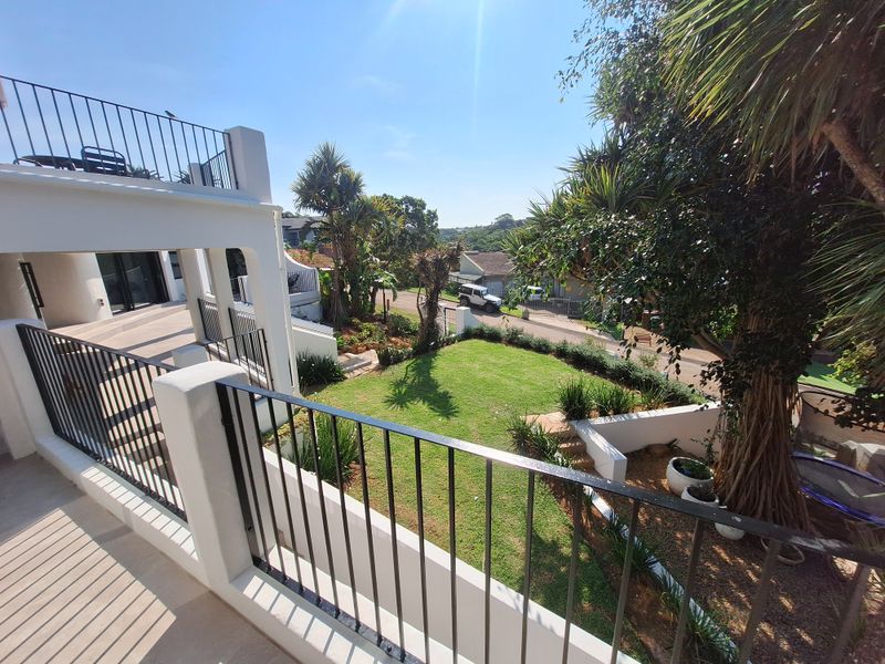 Elevated balcony overlooking a well-maintained garden and residential street, featuring modern metal balustrades and tiled flooring.