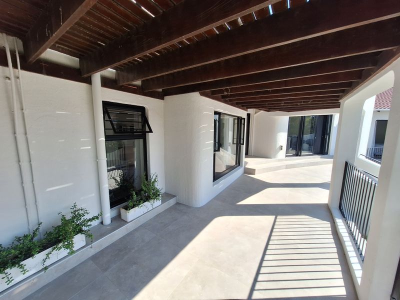 A spacious, modern covered patio featuring a timber pergola, sleek tiled flooring, and contemporary aluminium window and door frames.