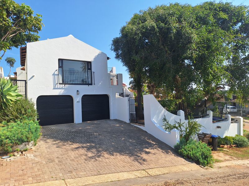 Front elevation of a two-story house featuring a double garage with roller shutter doors, a paved driveway, and an upper-level balcony.