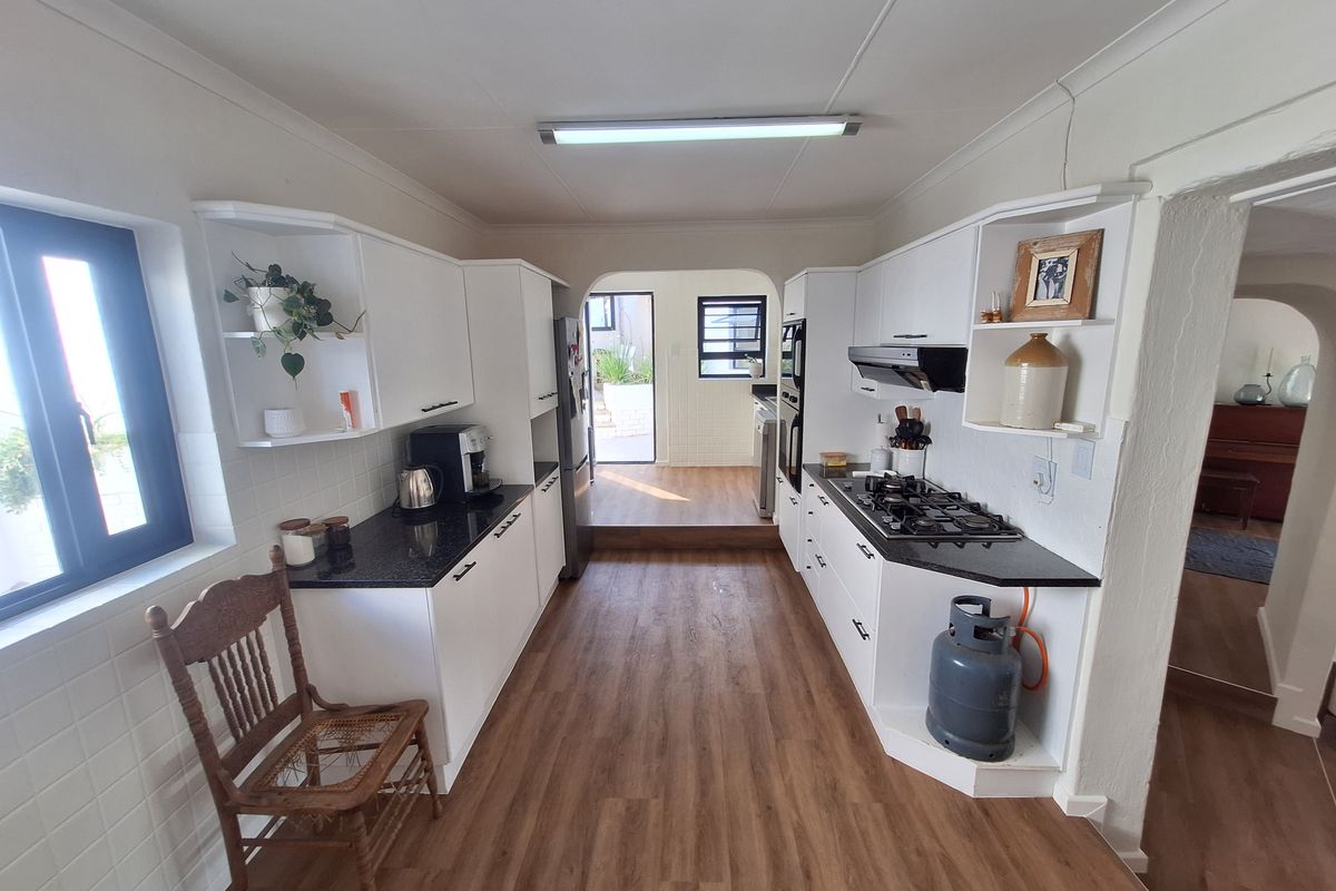 A functional galley-style kitchen featuring white cabinetry, granite countertops, a gas hob, and integrated oven, leading to an adjacent utility area.