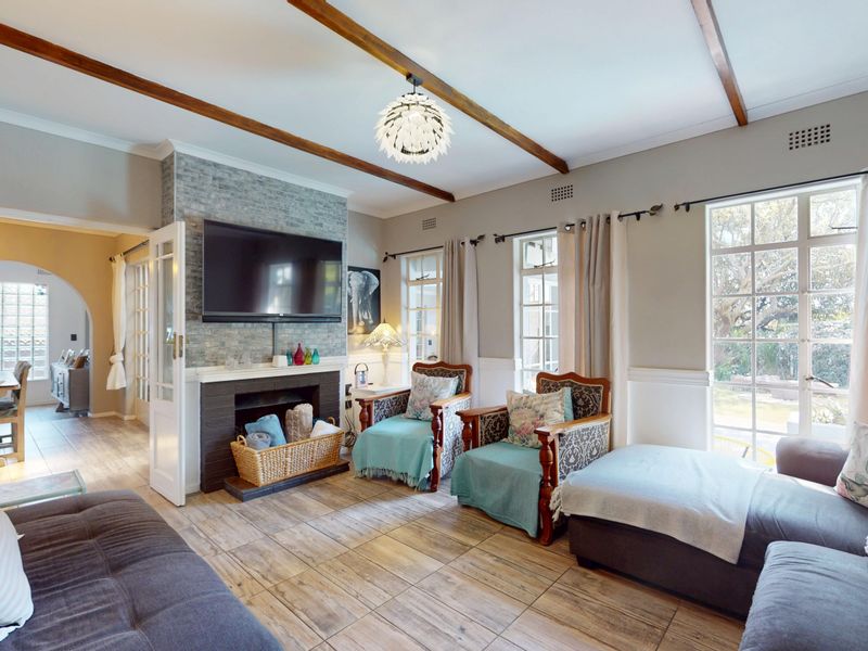 Spacious living room featuring exposed timber ceiling beams, a stone-clad fireplace, and tiled flooring with direct access to the garden through french doors.
