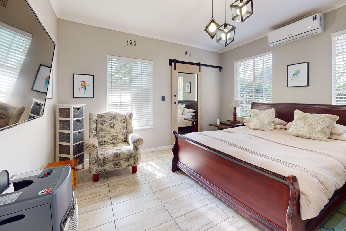 A well-maintained bedroom featuring tiled flooring, a sliding barn door, split-system air conditioning, and large windows with venetian blinds.