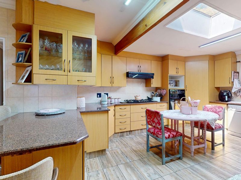 Spacious kitchen featuring light wood cabinetry, granite countertops, a gas hob, built-in oven, and a skylight providing ample natural light.
