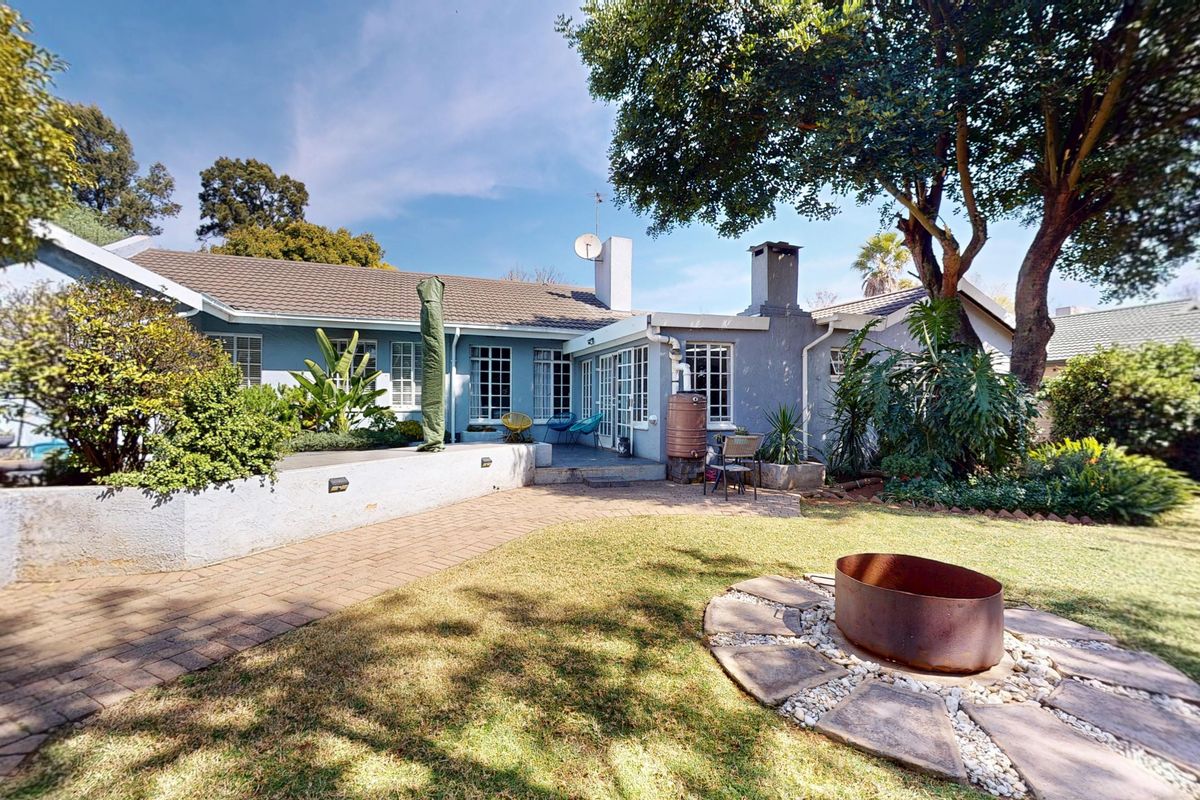 Rear view of the house featuring a paved patio area, a built-in fire pit, and a landscaped garden with mature trees.