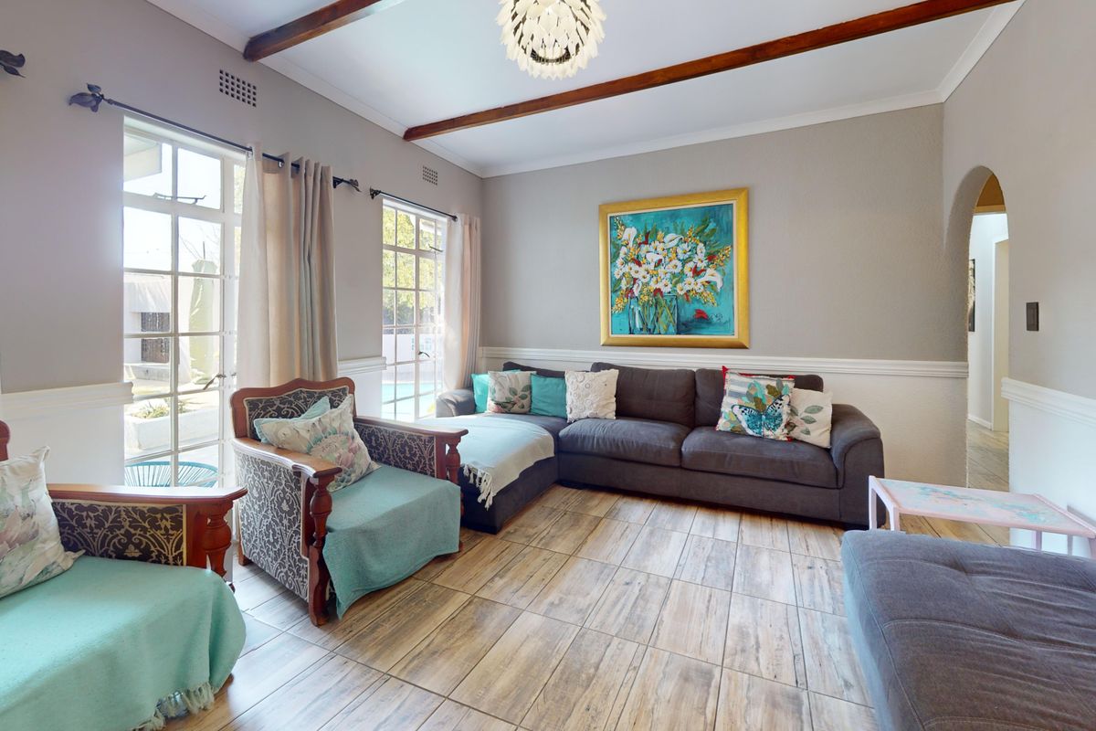 A comfortable living room featuring exposed timber ceiling beams, tiled flooring, and classic chair rail molding, with natural light flowing through the french doors.