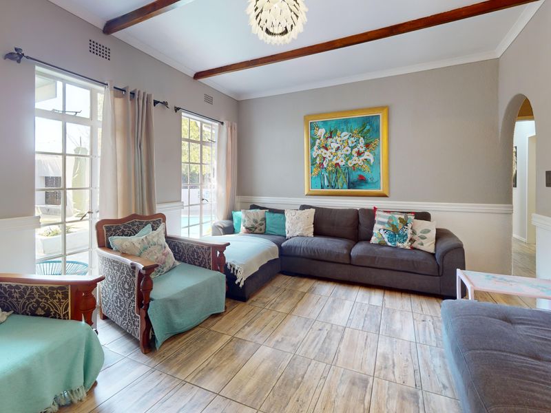 A comfortable living room featuring exposed timber ceiling beams, tiled flooring, and classic chair rail molding, with natural light flowing through the french doors.