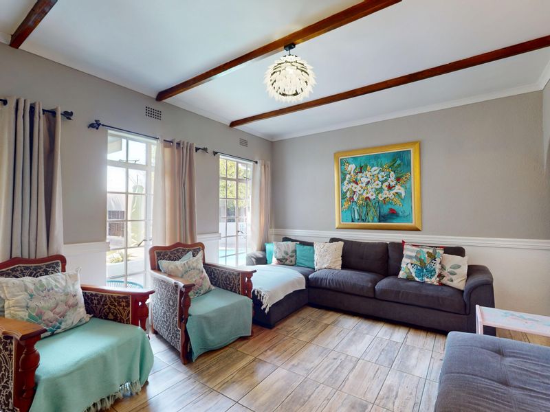 A bright living room featuring exposed timber ceiling beams, tiled flooring, and classic wainscoting, with direct access to the outdoor area through french doors.