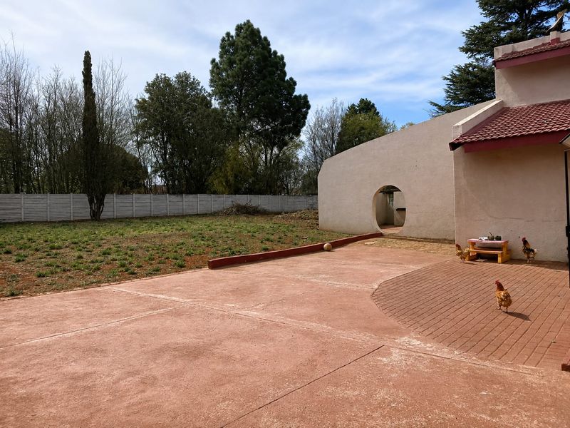 Spacious rear exterior area featuring a combination of concrete and brick paving, a unique circular wall opening, and a large private garden.