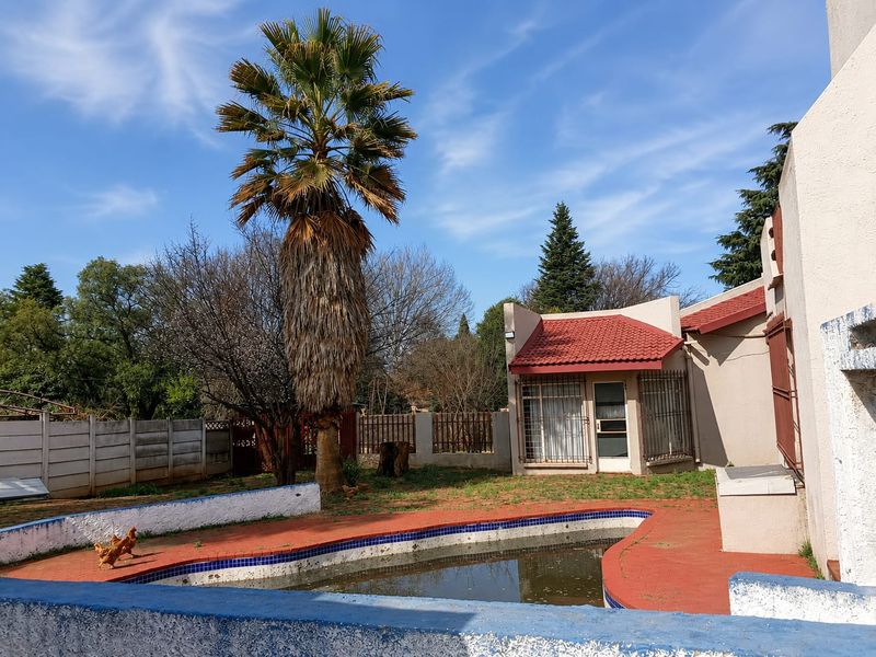 Rear garden area featuring a swimming pool with tiled surround, security bars on windows, and a precast concrete boundary wall.