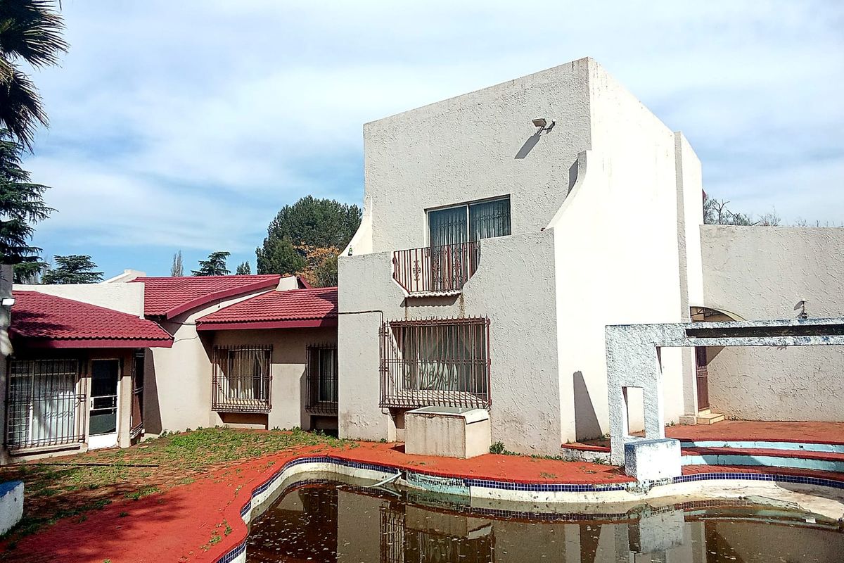 Rear exterior view of a multi-level house featuring a swimming pool, balcony, and security bars on windows, requiring significant maintenance and pool restoration.