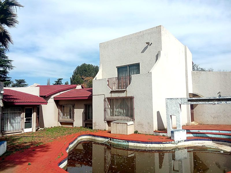 Rear exterior view of a multi-level house featuring a swimming pool, balcony, and security bars on windows, requiring significant maintenance and pool restoration.