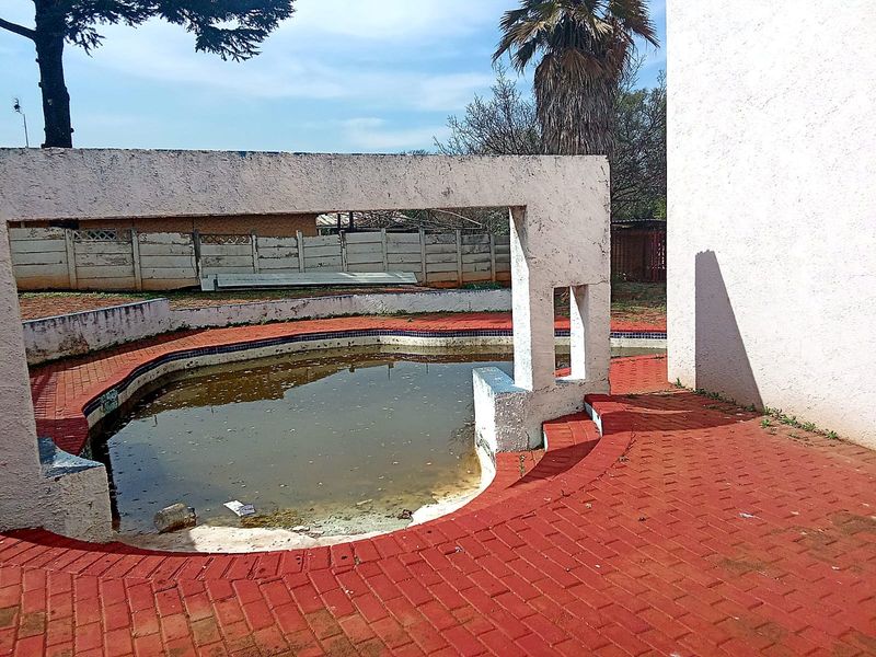 Outdoor pool area featuring a concrete pergola structure and red brick paving, currently requiring significant maintenance and pool restoration.